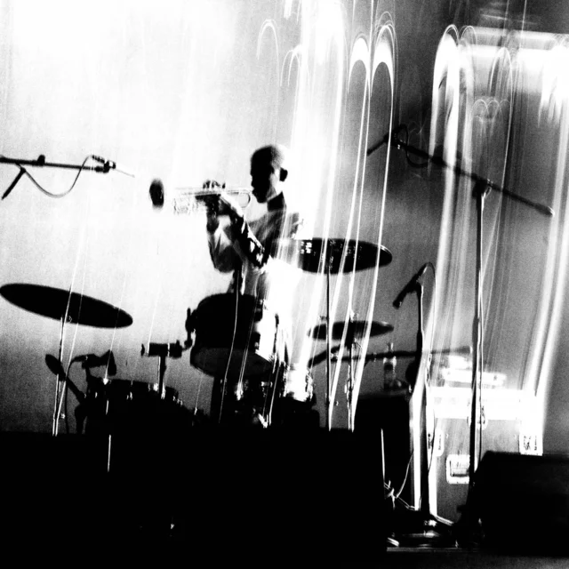 Drummer performing on stage behind a drum kit with microphones and light streaks in black-and-white.