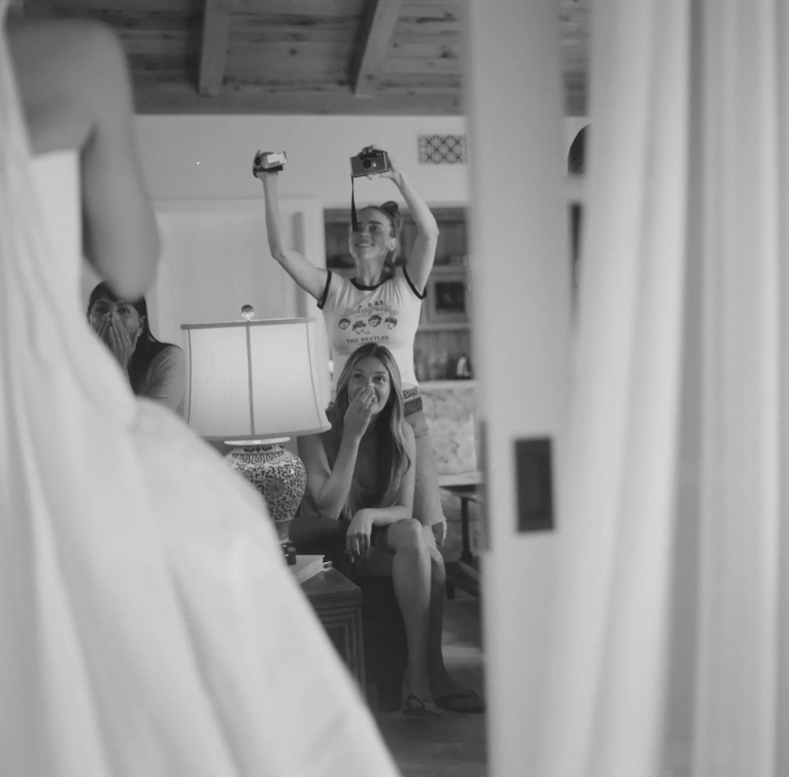 Woman with a camera raised overhead, smiling, as others watch indoors.