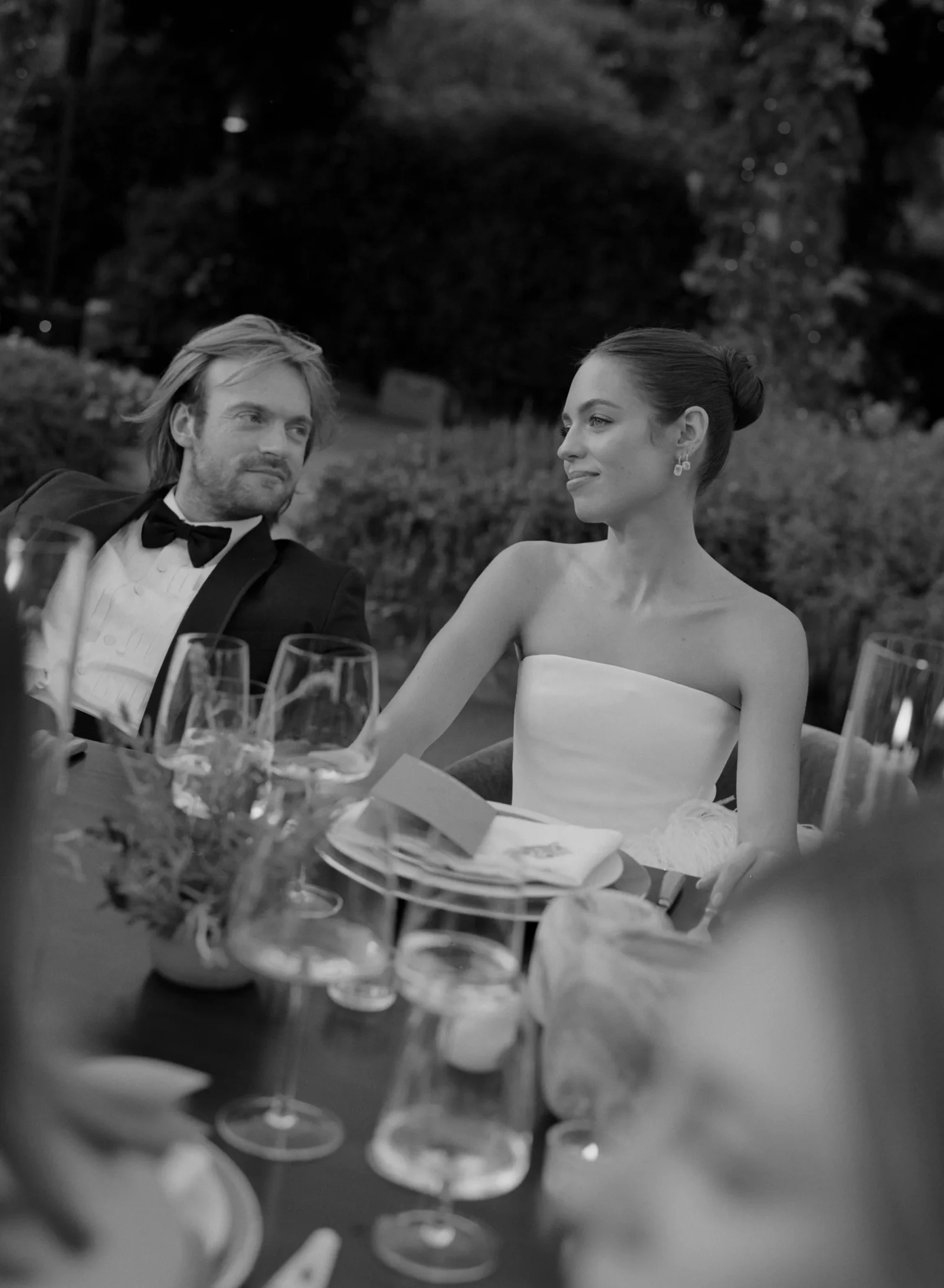 A formally dressed couple toasting with wine glasses at an outdoor wedding reception.