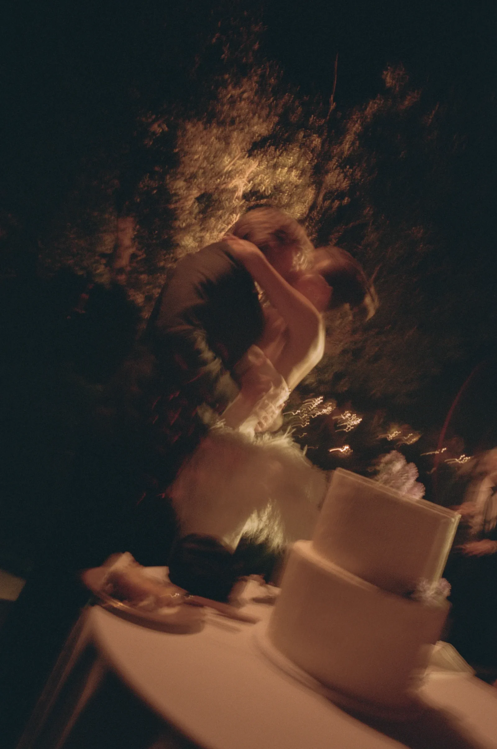 Couple kissing in a dimly lit outdoor setting with warm, amber lighting and motion blur.