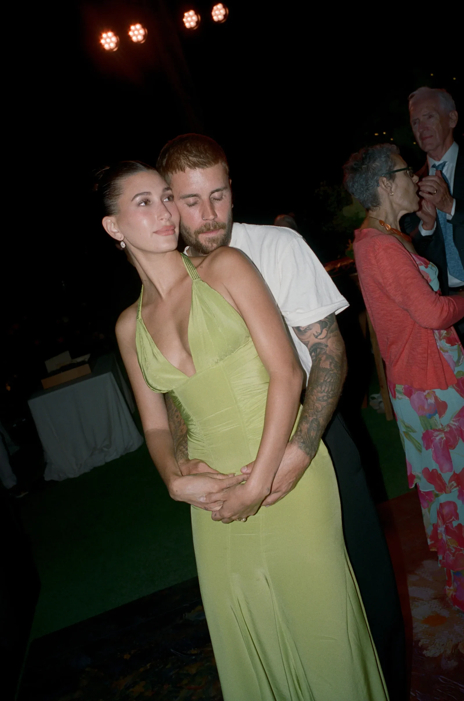 A couple embracing on a dance floor at night: woman in a lime-green dress with the man standing behind her, eyes closed.