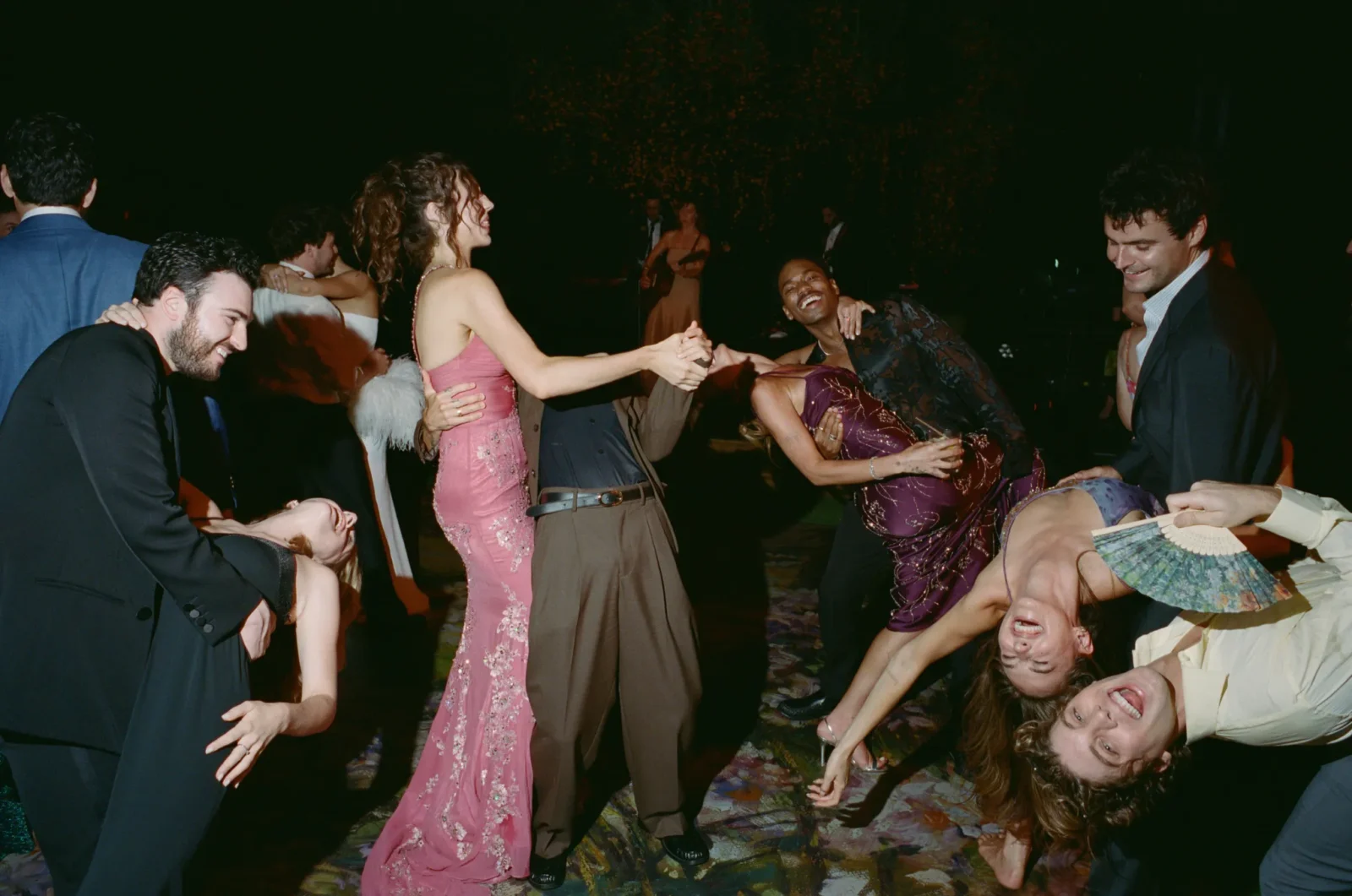 Guests in formal attire dancing and laughing at a nighttime party on a crowded dance floor.