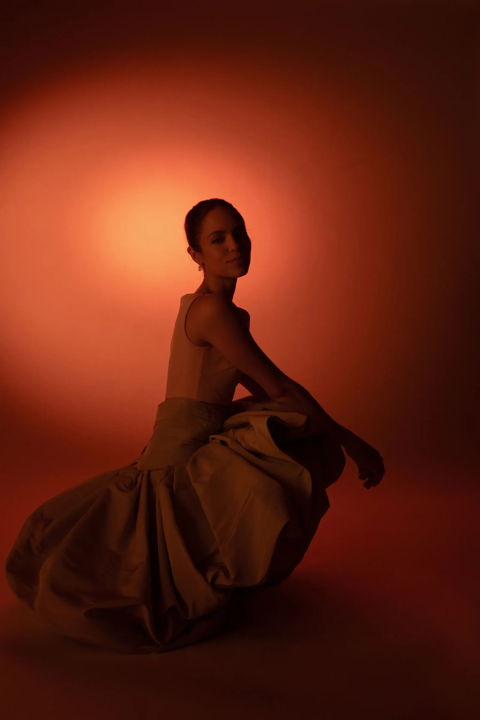 Silhouette of a woman in a flowing dress posed sideways against a warm orange backdrop.