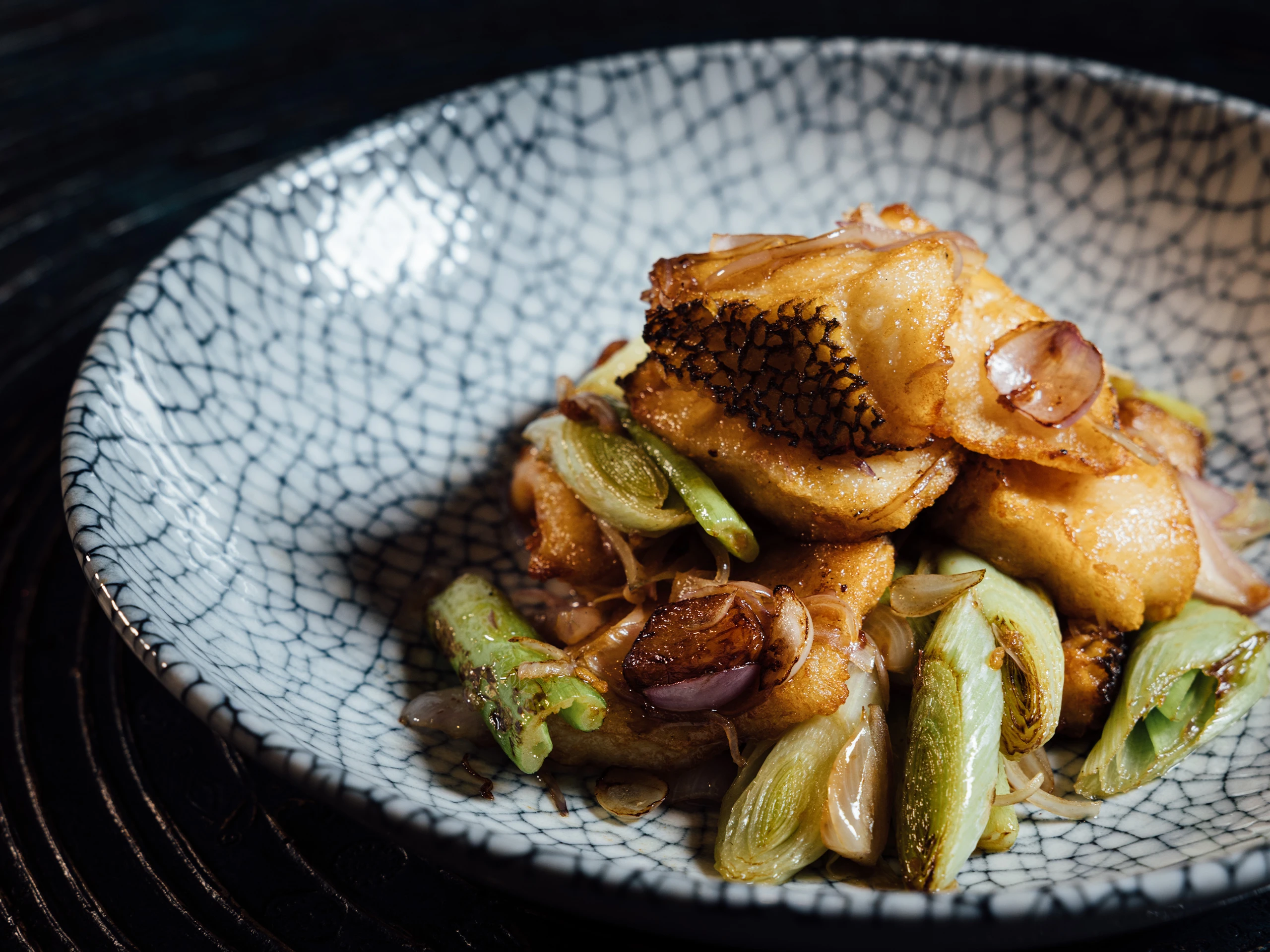 Crispy fried fish skin resting on sautéed onions and greens on a blue crackle-patterned plate.
