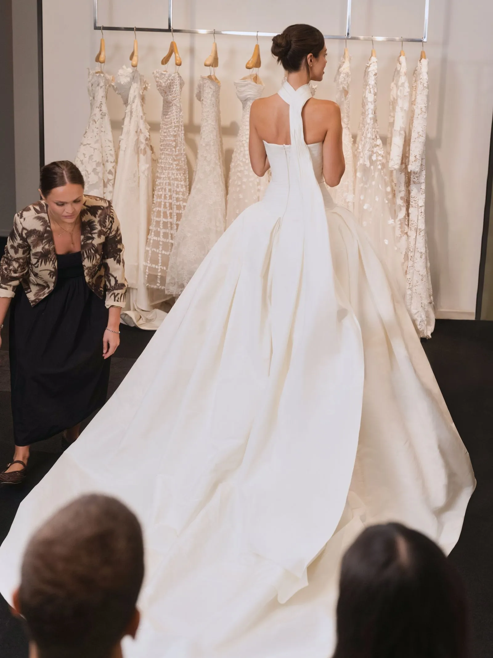 Bride-sized white wedding gown on a model with back exposed, surrounded by lace dresses on a rack, in a fitting room.