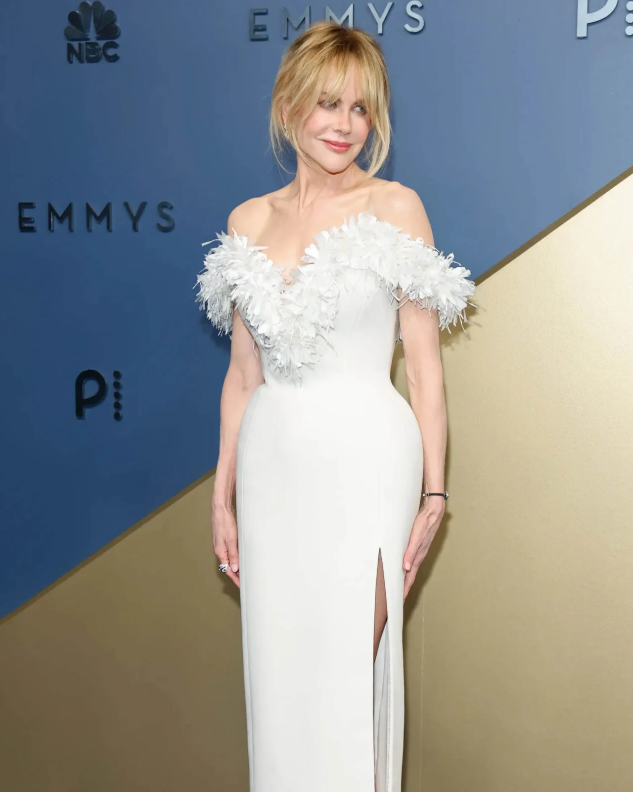 Smiling woman in a light blue dress posing against a blue backdrop with Emmy logos in the background.