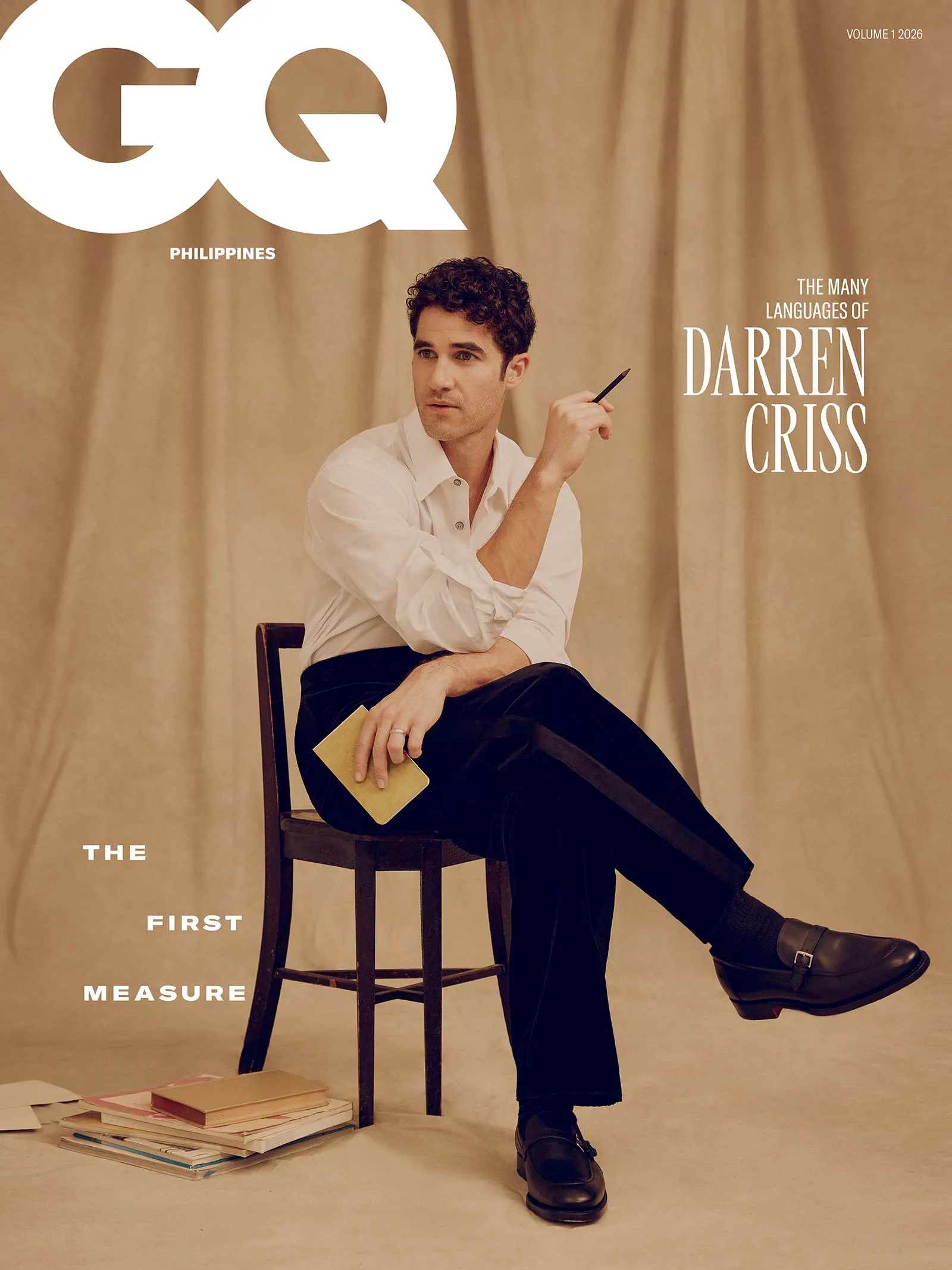 GQ Philippines magazine cover featuring a man in a white shirt sitting on a chair, holding a pencil, with notebooks on the floor and beige curtains in the background.