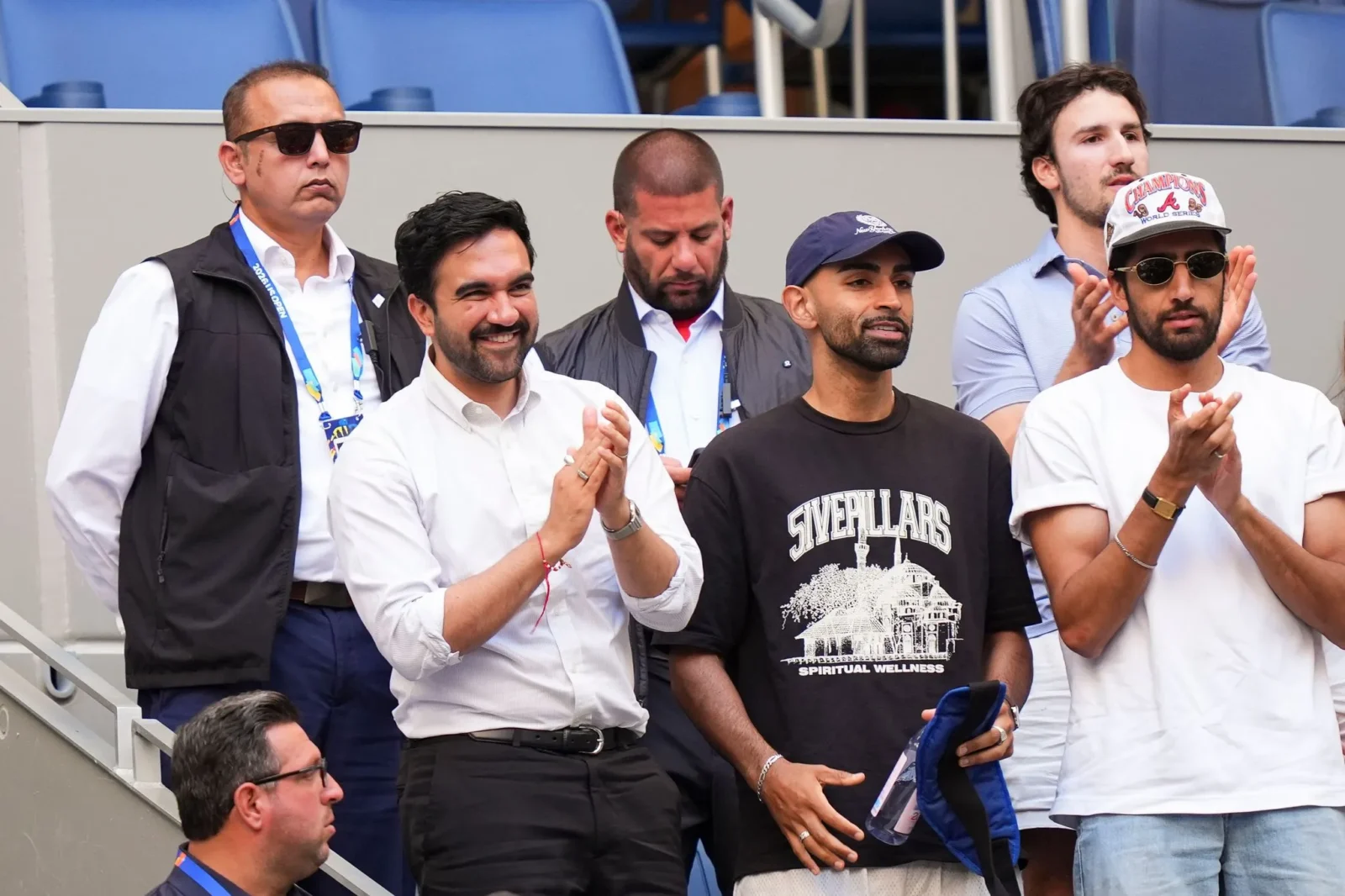Group of men standing and clapping in stadium seating during an event.