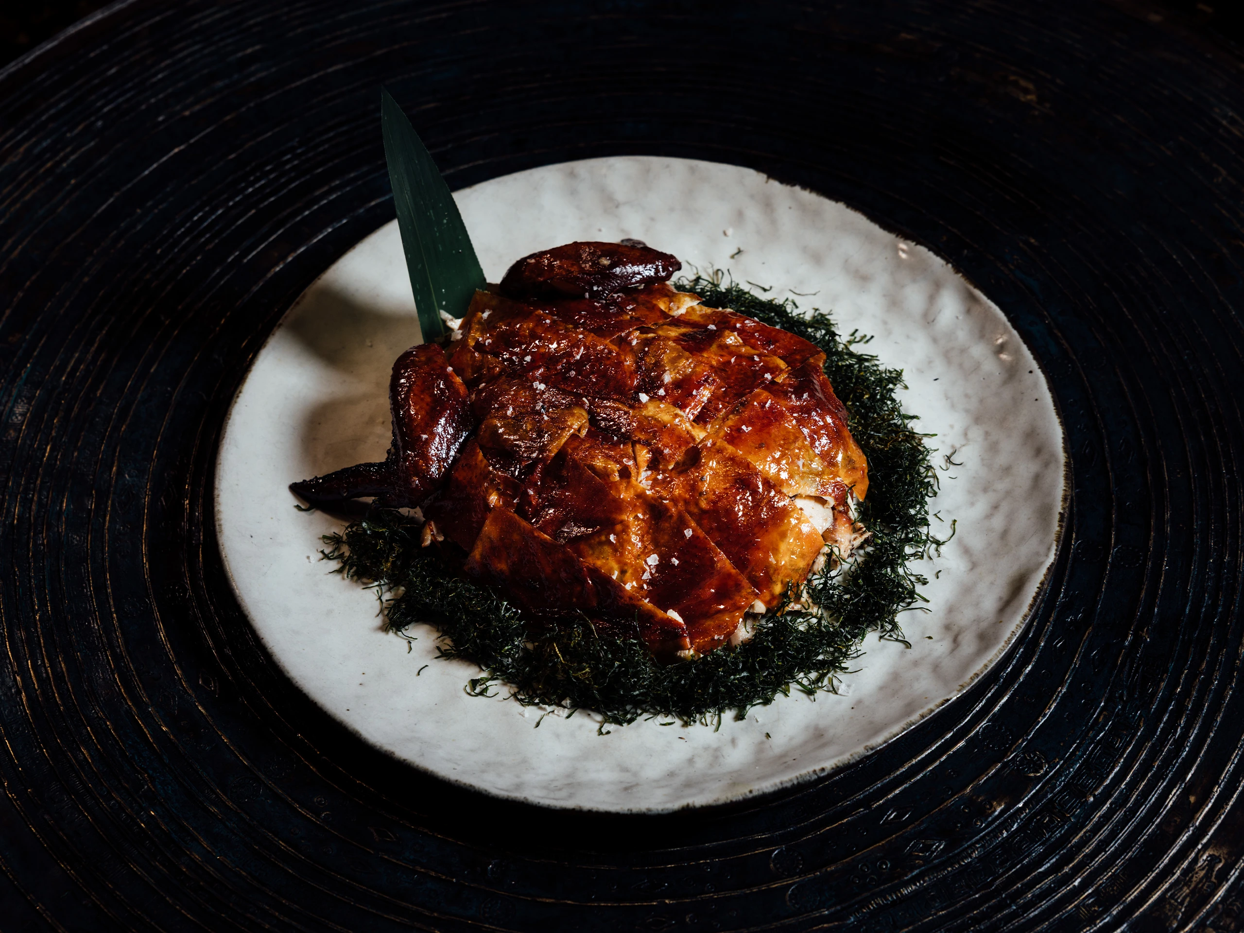 Roasted glazed meat on a white plate surrounded by dark greens, plated for a dinner dish.