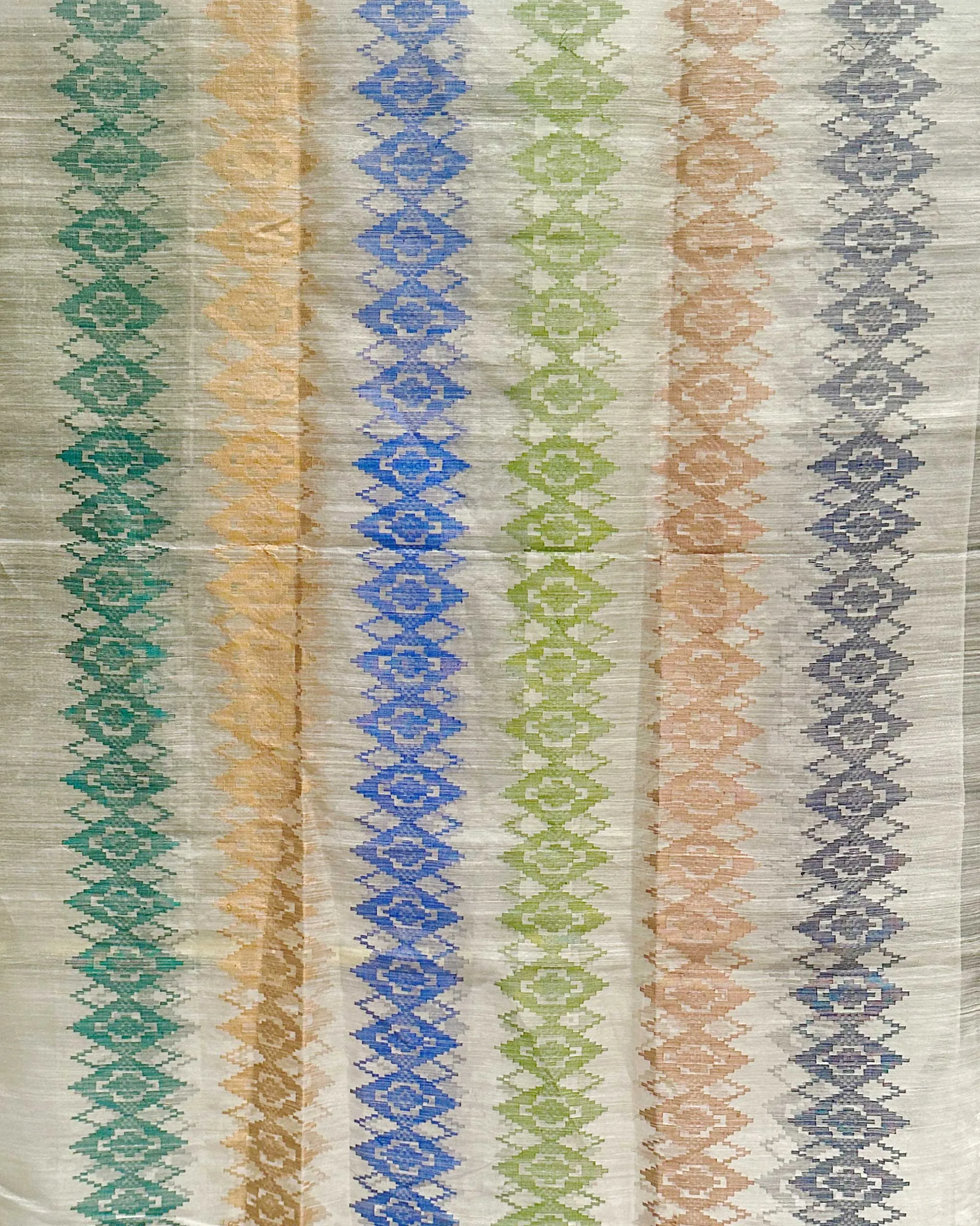 Vertical stripes of diamond motifs in teal, yellow, blue, green, peach, and gray on a light woven rug.