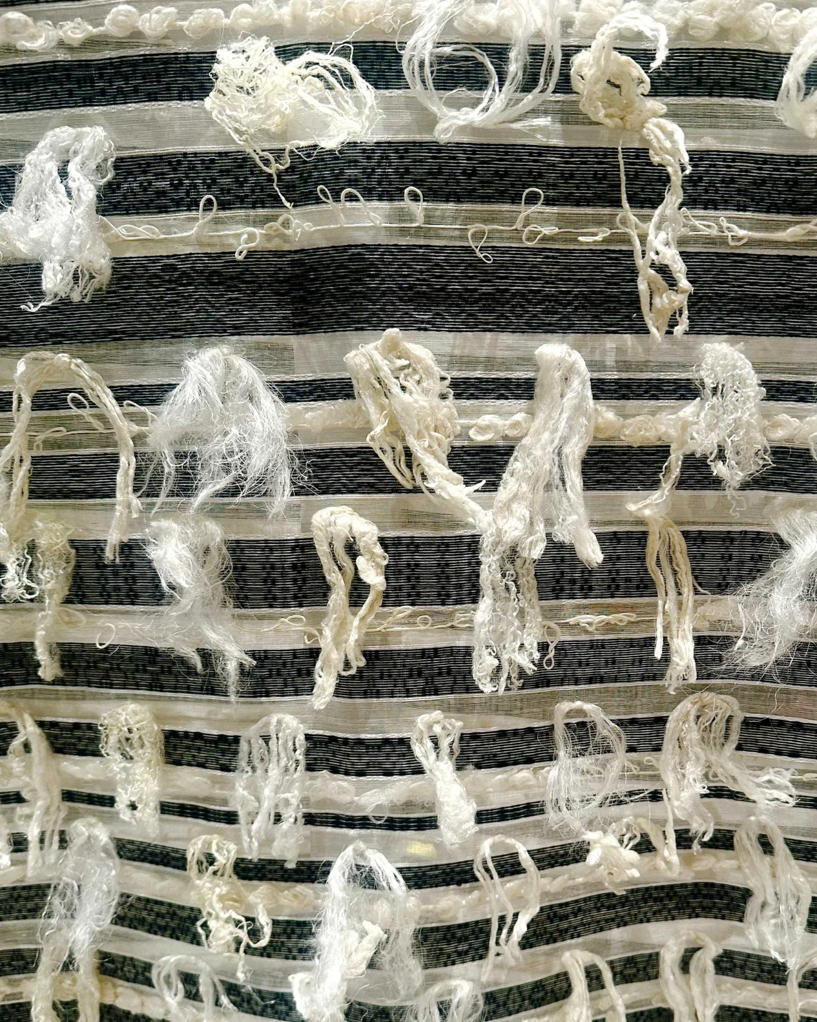 Close-up of striped fabric (black and white) with scattered frayed white yarns and knotted strands.