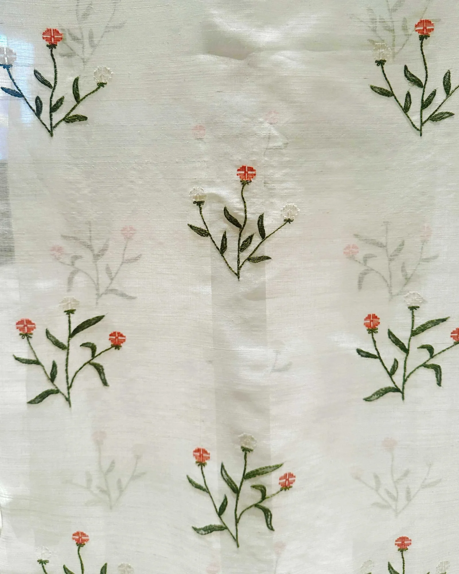 Cream-colored fabric featuring embroidered green stems and small red blossoms scattered across the pattern.