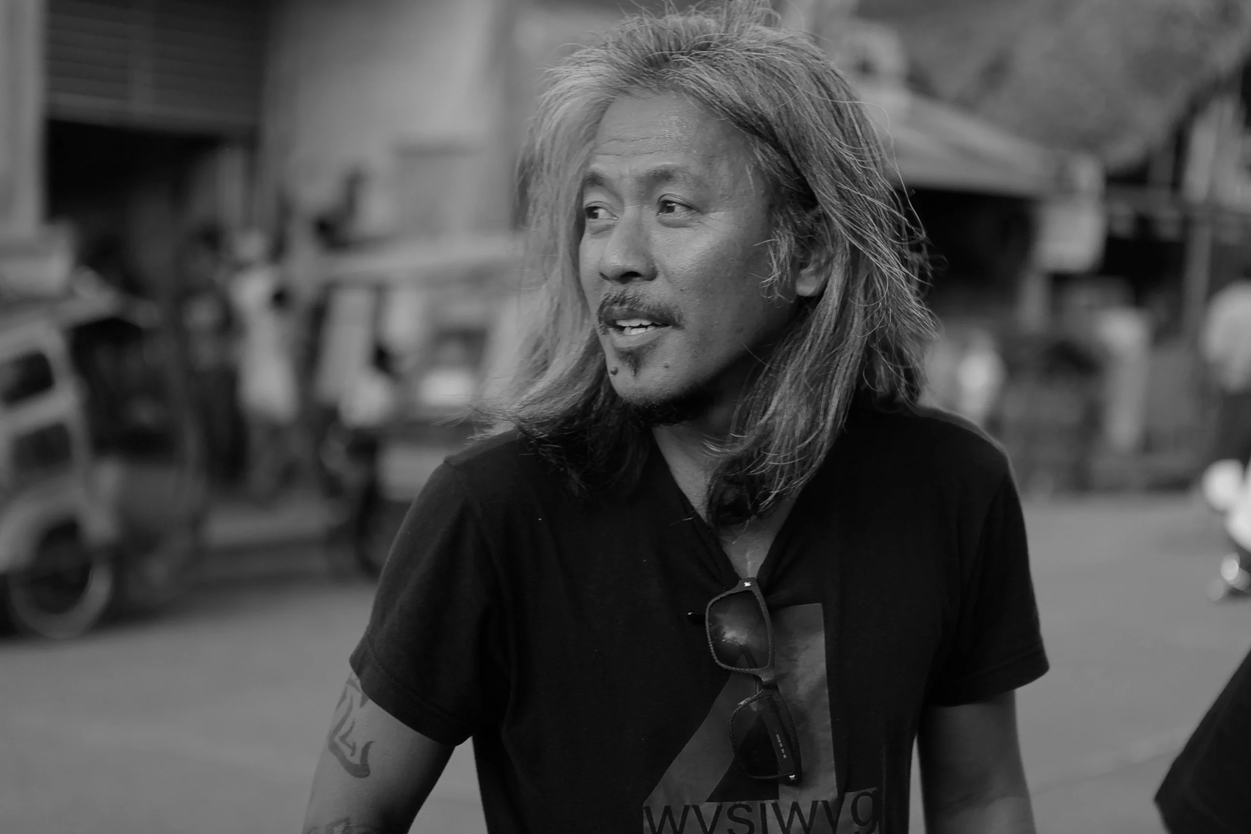 Black-and-white portrait of a man with long hair looking to the left on a street background.