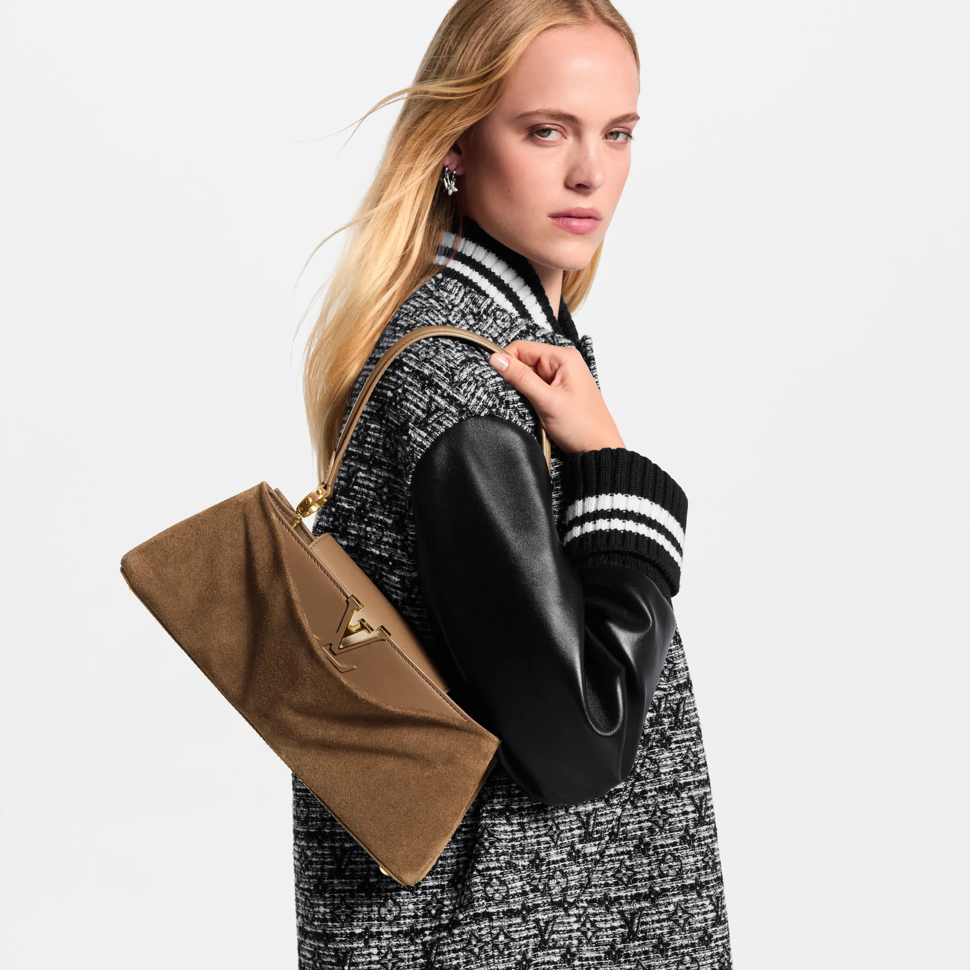 Model posing with a tan suede handbag over the shoulder, wearing a black-and-white textured coat with leather sleeves.