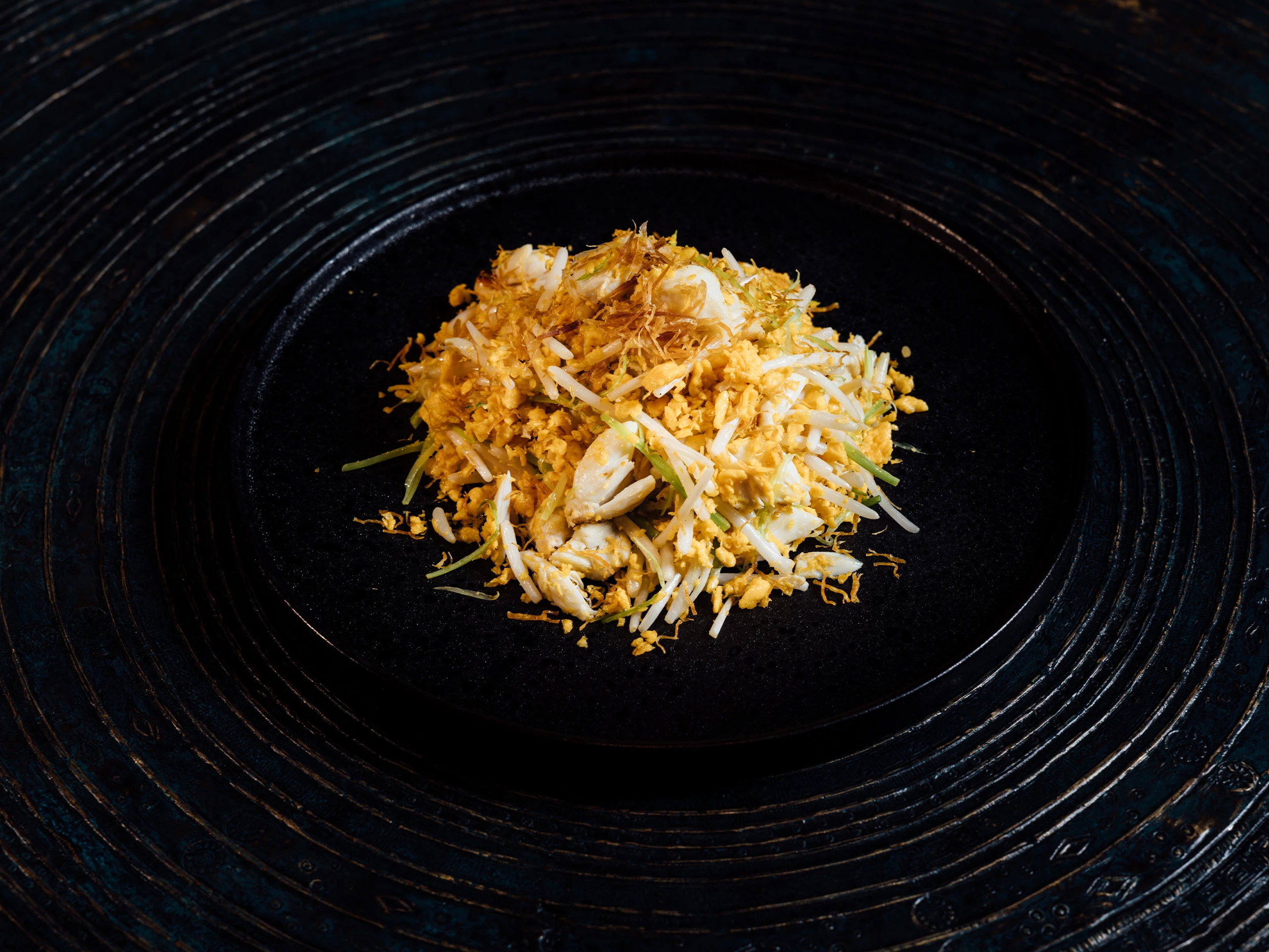 Pile of scrambled eggs with bean sprouts and thinly sliced green onions on a dark plate.