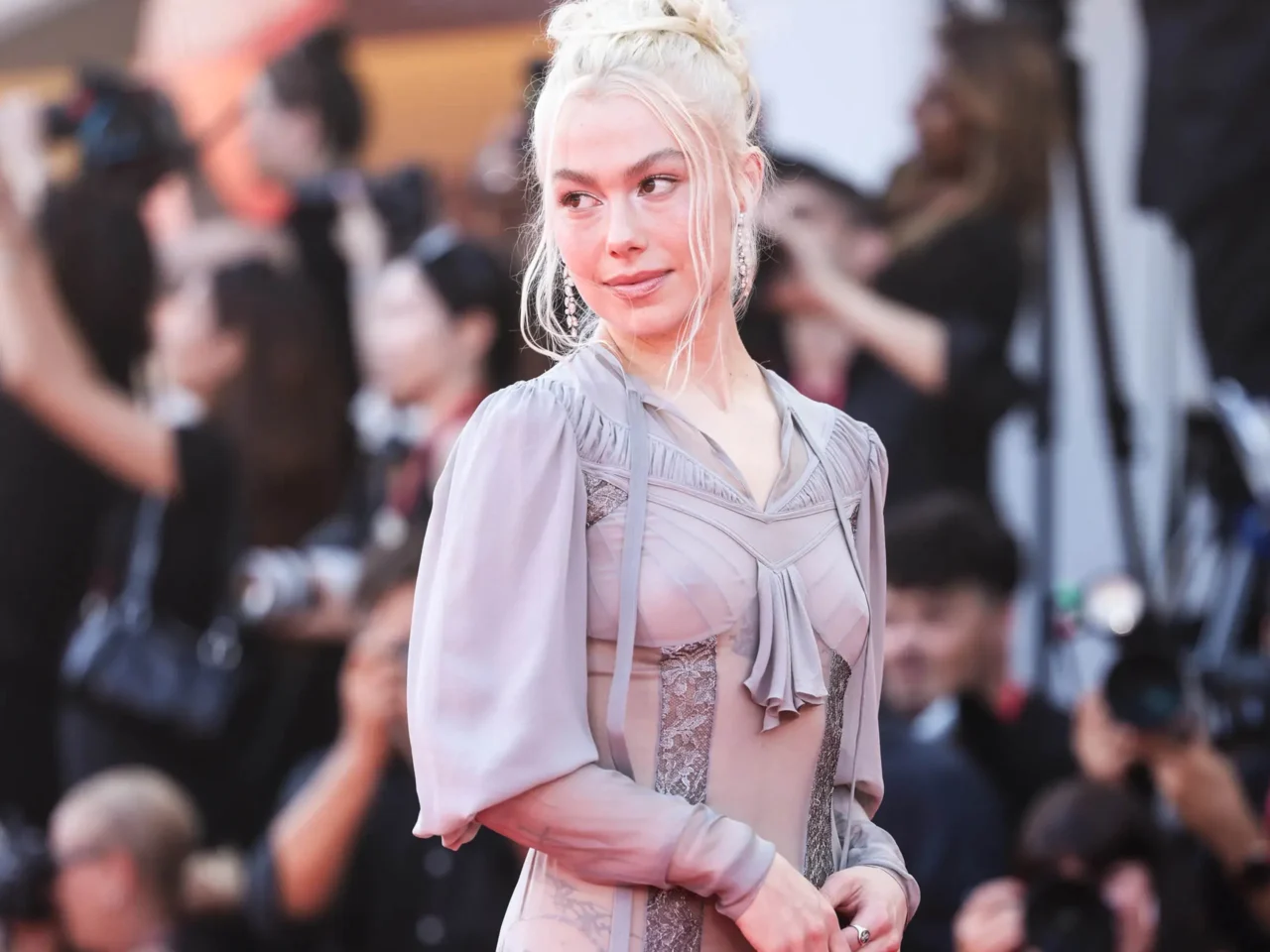 Portrait of a stylish blonde woman in a light lavender outfit at a crowded event, looking to the side.