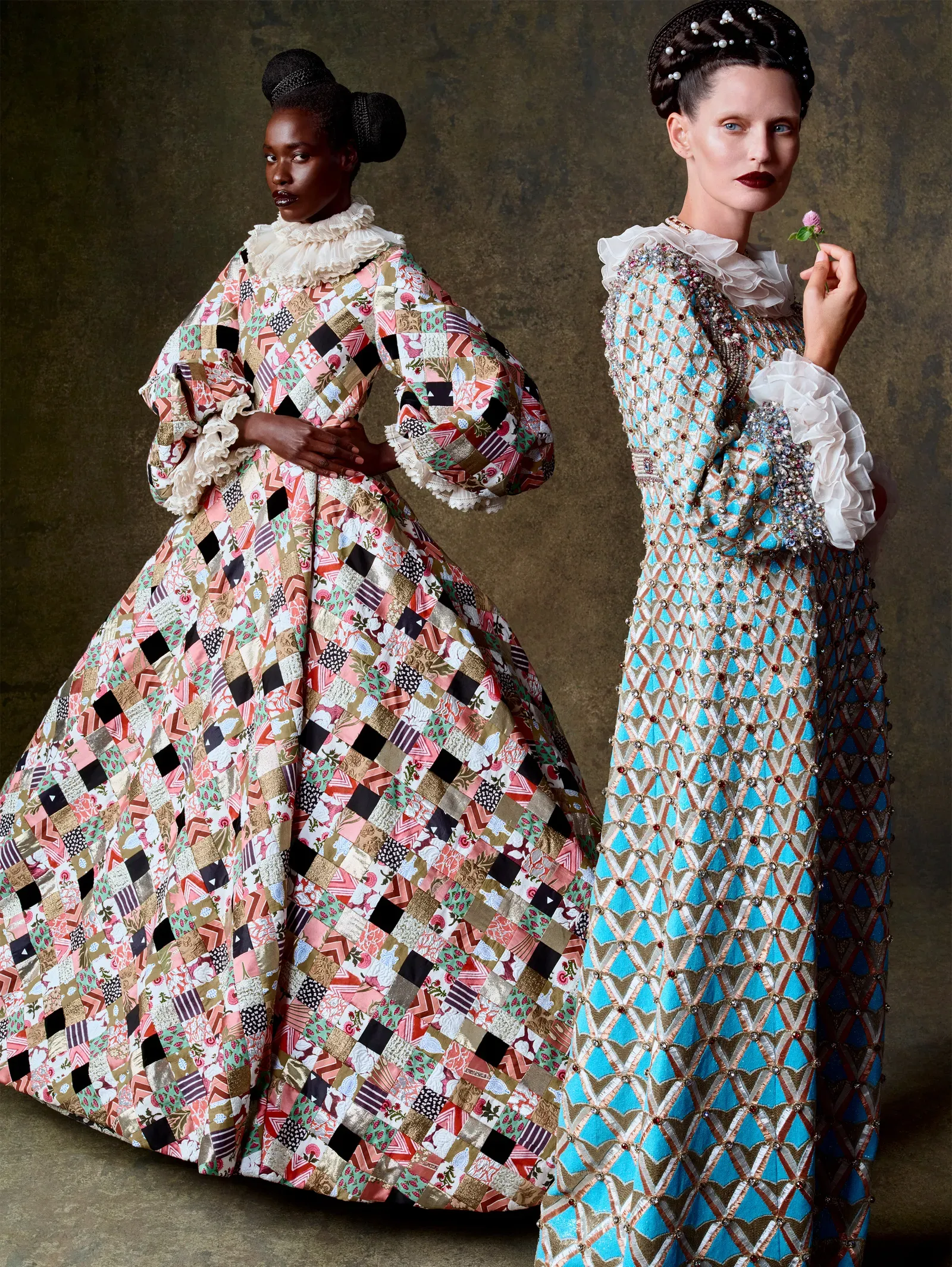 Two models in extravagant, patchwork-style gowns pose against a textured backdrop; one in a voluminous quilted dress, the other in a blue lattice gown holding a small flower.