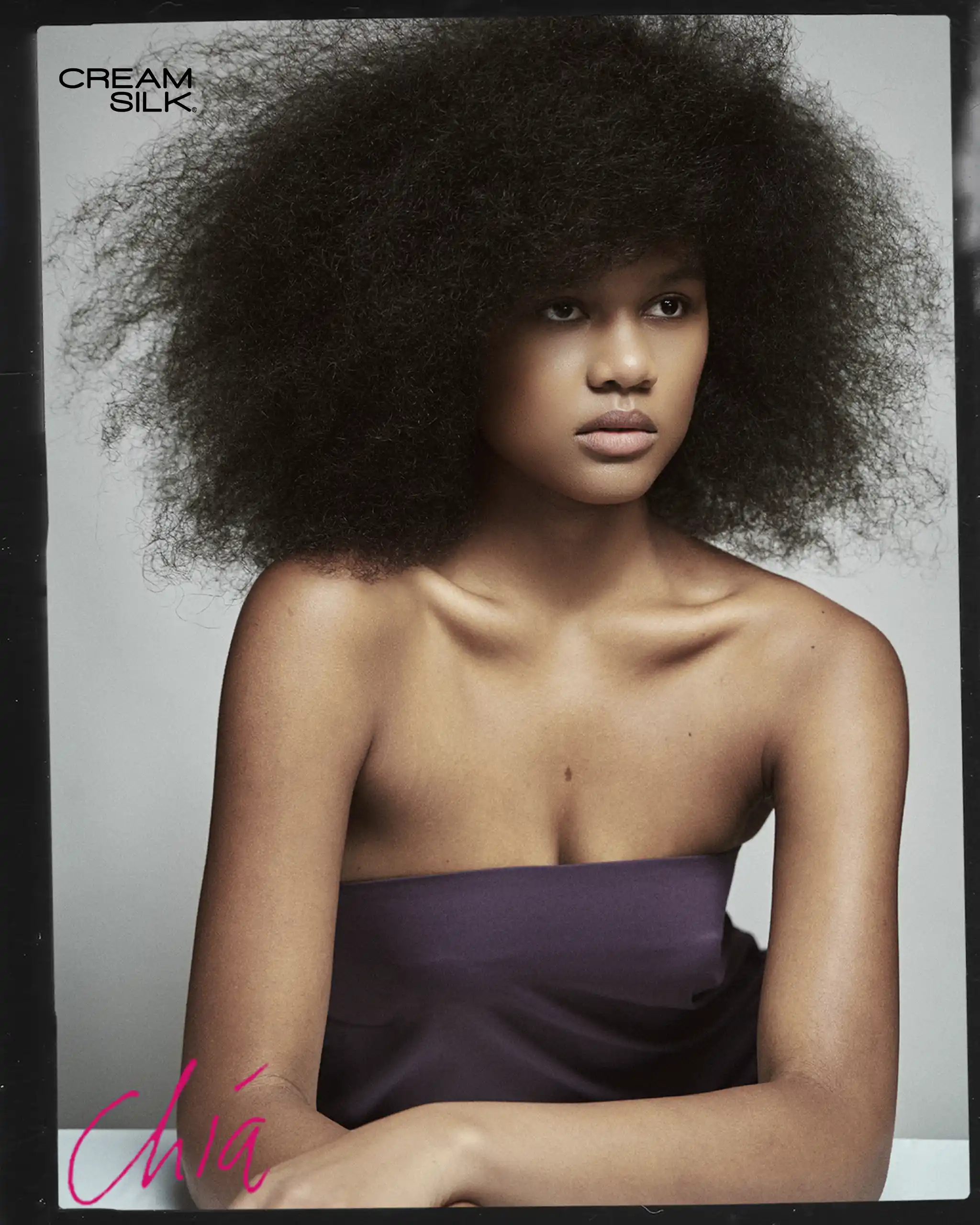 Portrait of a woman with a large natural afro, bare shoulders, wearing a purple strapless top; Cream Silk logo in the upper left corner.