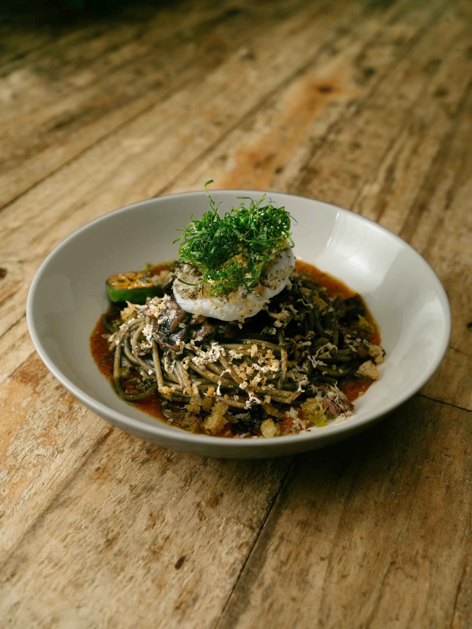 Bowl of pasta with tomato sauce, melted cheese, crispy crumbs, and a sprig of fresh herbs on a rustic wooden table