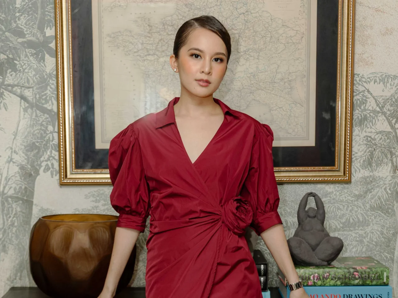 Woman in a red blouse posing in front of a framed vintage map wall art.