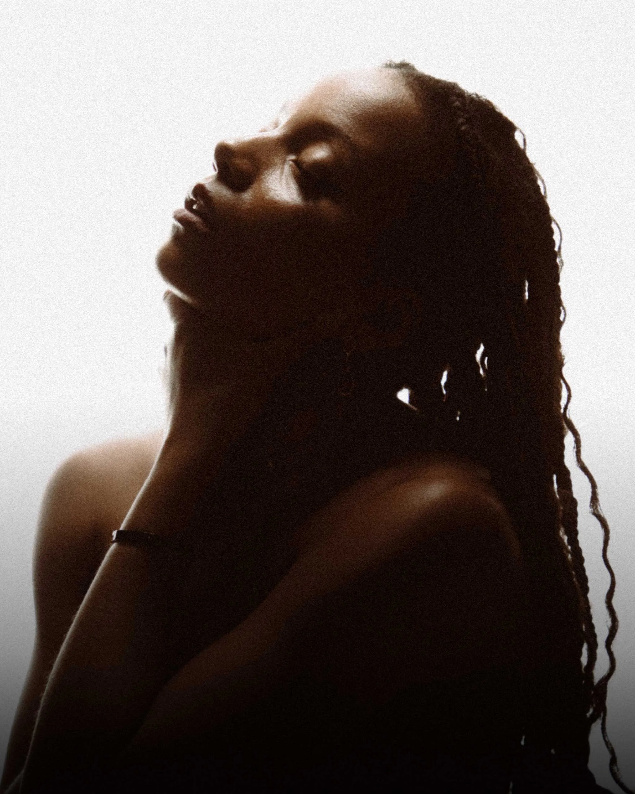 Silhouette of a person with dreadlocks, head tilted back in profile against a pale background.