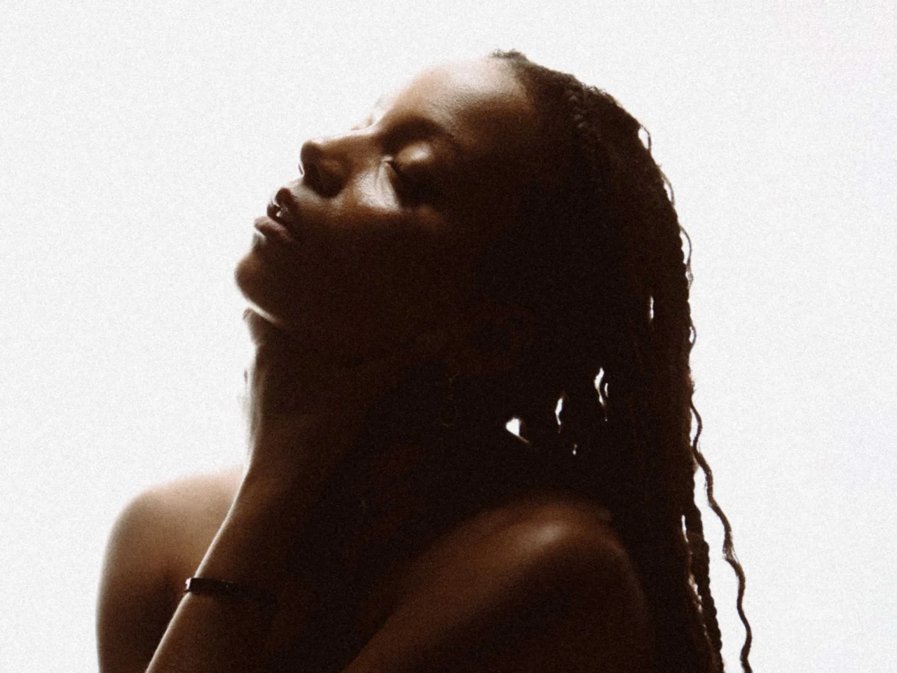 Silhouette of a person with dreadlocks in profile, head tilted back against a bright pale background.