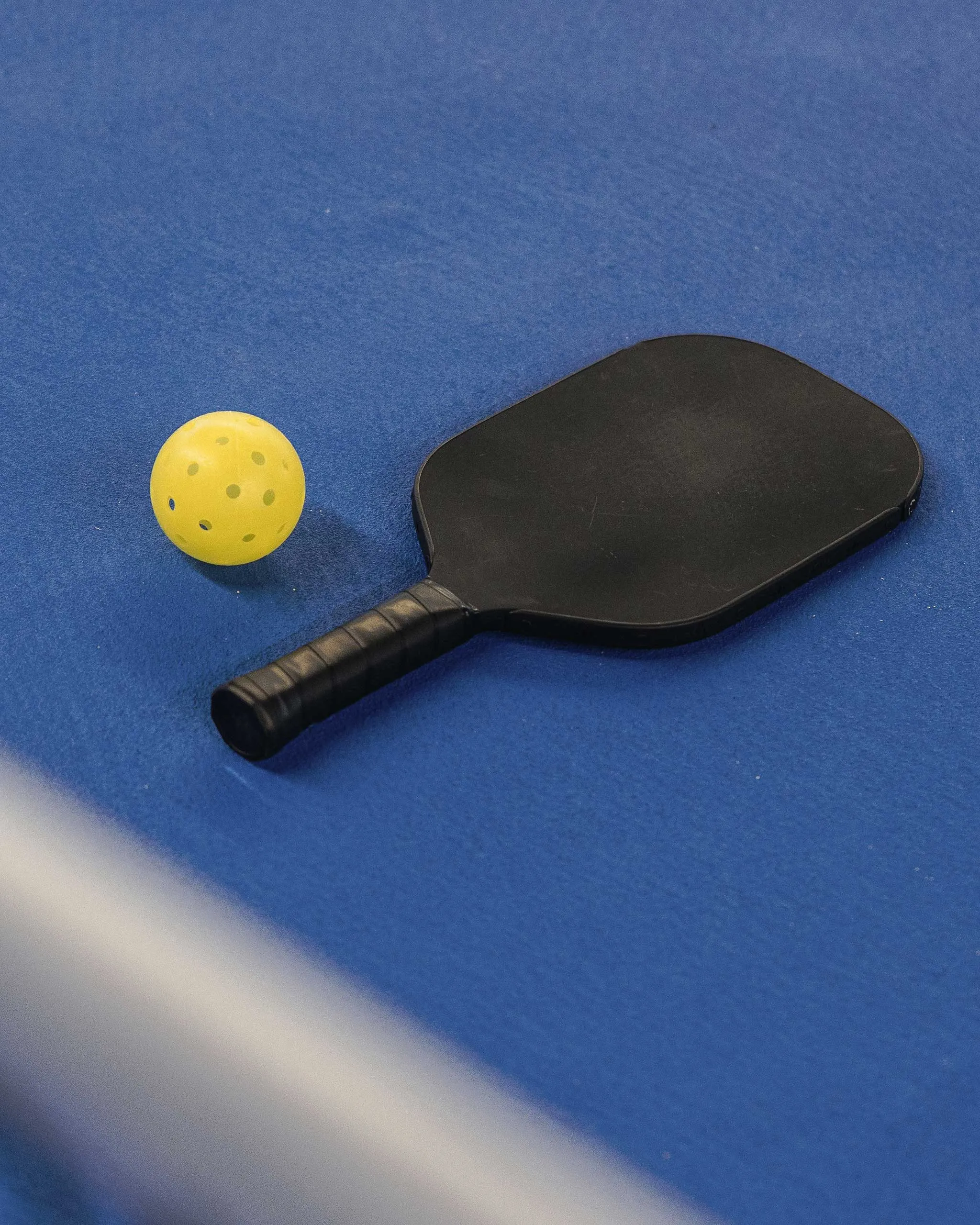 Yellow perforated ball next to a black table tennis paddle on a blue playing surface