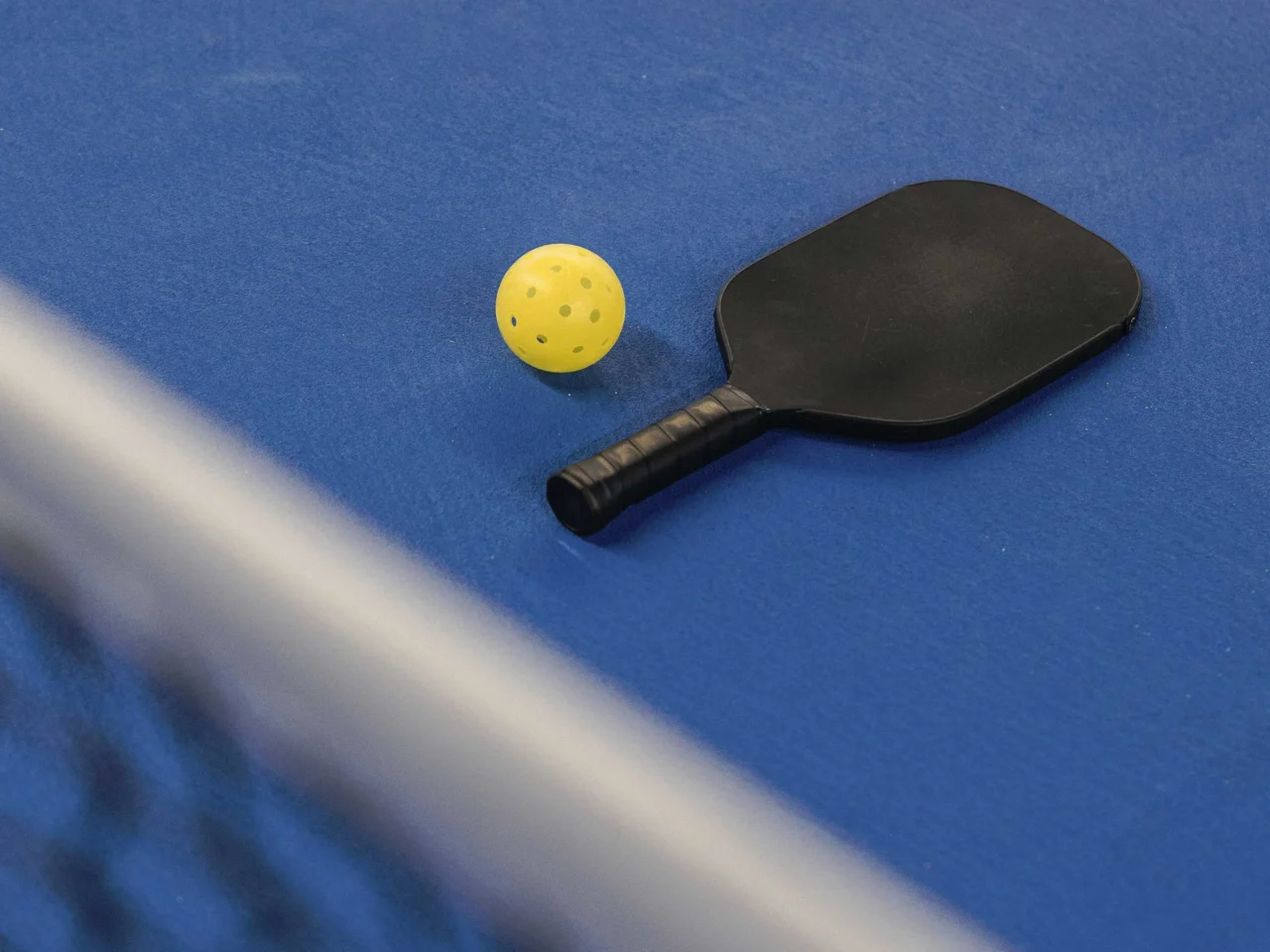 Yellow ping-pong ball next to a black paddle on a blue table tennis surface on the right side of the image.