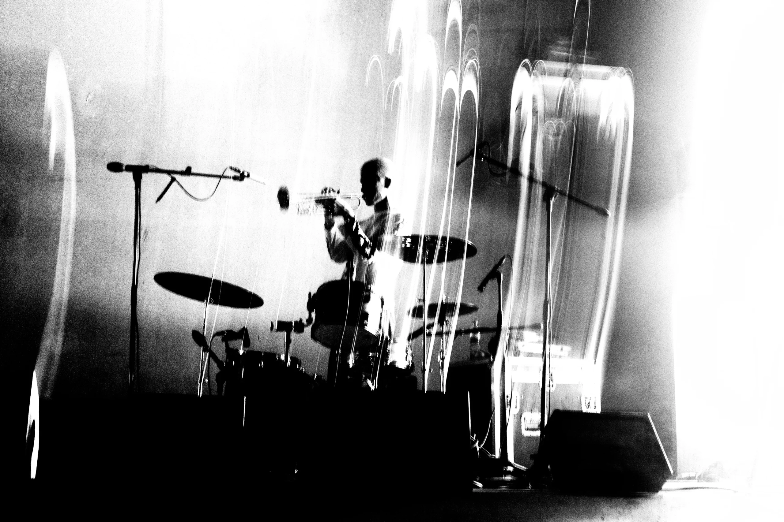 Drummer performing on stage with a full drum kit and multiple microphones in a high-contrast black-and-white photo.