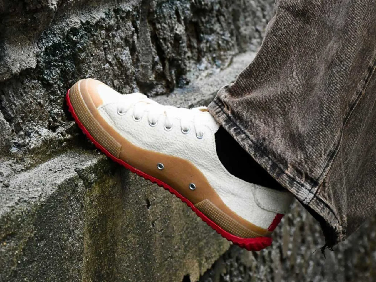 White sneaker with tan sole stepping on rocky surface, denim jeans visible at the ankle.
