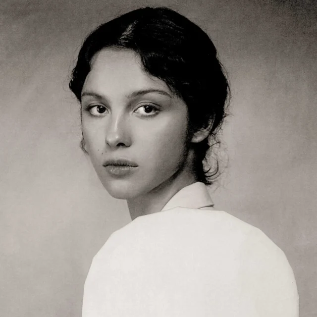 Black-and-white portrait of a woman with short dark hair, looking toward the camera, wearing a light-colored top.