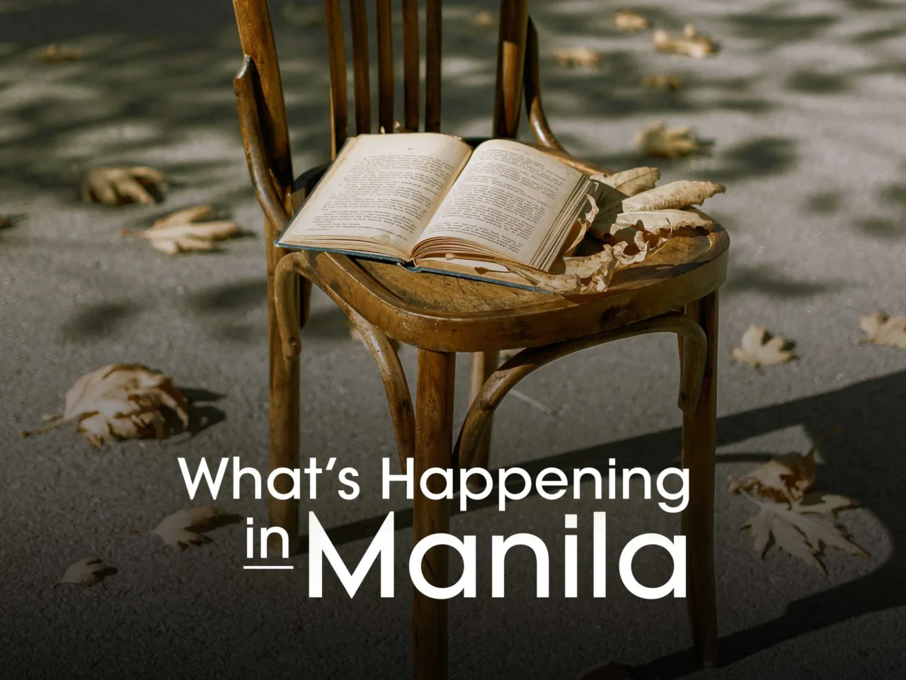 Wooden chair with an open book on the seat on a street, autumn leaves scattered, overlaid with the text “What’s Happening in Manila.”
